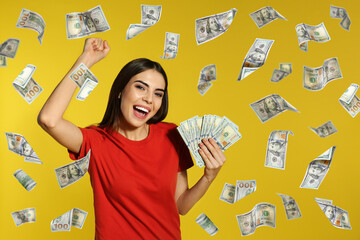 Happy young woman with money and falling American dollars on yellow background