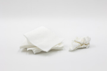 white square paper napkins in a pile and one crumpled used ones lie nearby isolated on a white background