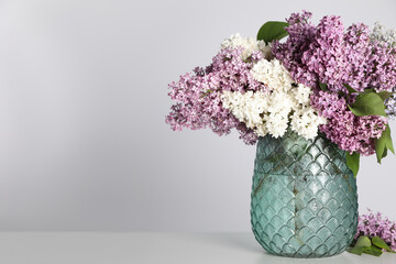 Beautiful lilac flowers in glass vase on light background. Space for text