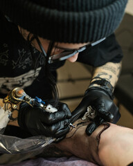 Fototapeta na wymiar Professional tattoo artist stuffs a tattoo on the man's hand. Tattoo artist at work. Tattoo creation process. Art and creativity