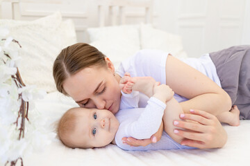 portrait of a mother with a baby, a mother gently embraces a child on a white bed at home, maternal love and care