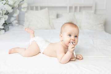 baby with a pacifier in diapers on a white cotton bed at home six months old