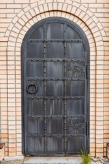 An old iron door in the shape of an arch, a forged door made of durable metal, a brick wall with an...