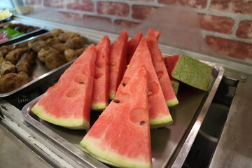 Red watermelon sliced into triangles stacked and displayed on an iron plate
