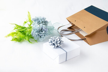 美しいブルーグレーのダリアの花束と銀色のリボンのプレゼントと青とベージュのショッピングバッグ（白バック）