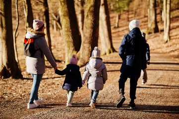 Back of mother with four kids wear jacket and hat in early spring forest.