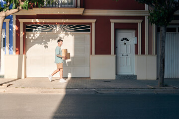 Young moving man with boxes in his hands in front of a house