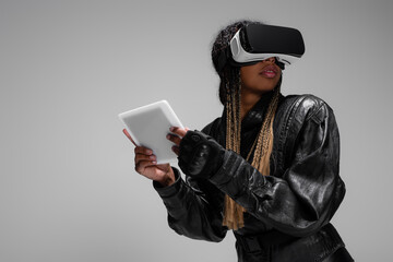 African american woman in vr headset holding digital tablet while gaming isolated on grey.