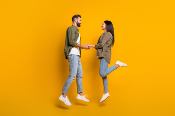 Full body profile side photo of young couple hold hands jump romance isolated over yellow color background