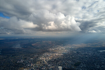 Aerial view from airplane window at high altitude of distant city covered with puffy cumulus clouds forming before rainstorm