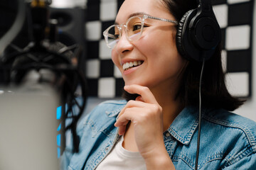 Beautiful happy young female radio host using microphone and headphones while broadcasting in studio