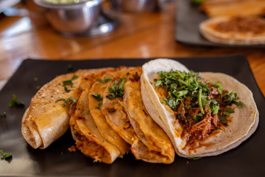 Tacos de birria con cilantro y tortilla de maíz, salsa barbacoa, platillo típico de México, comida mexicana deliciosa en plato de barro negro