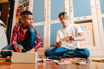 Two young teenagers sitting on floor and doing name tags in bedroom