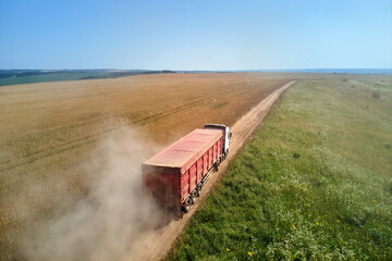 Aerial view of cargo truck driving on dirt road between agricultural wheat fields making lot of...