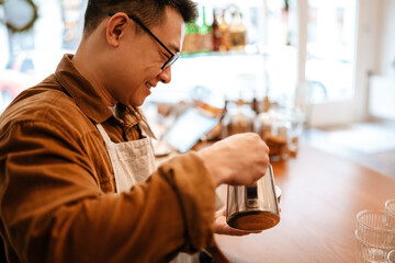 Adult asian man wearing apron making coffee while working in cafe