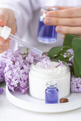 Obraz na płótnie Canvas Female scientist doing laboratory research with natural organic essential oils and flower extracts. Lilac for anti-age and anti-acne therapy, moisturizing. White background.