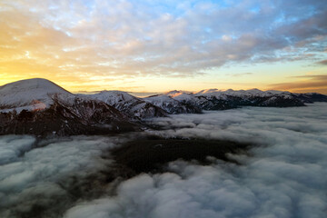 Aerial view of vibrant sunrise over white dense clouds with distant dark mountains on horizon