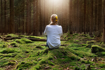 Woman sitting in green forest enjoys the silence and beauty of nature.
