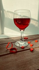 Glass of red wine, red hearts and red oil candle isolated on white background, calm afternoon, sunlight reflecting on white wooden table, Saint Valentines Day,  sitting view