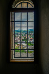 Large antique window in an 18th century castle  that shows a beautiful natural landscape with branches, leaves, trees and a cloudy blue sky and mountains