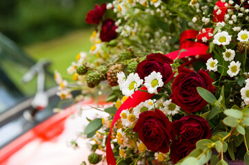 Bouquet of roses, daisies and other wild flowers as wedding decoration on a red vintage car