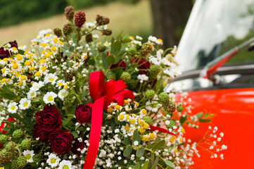 Bouquet of roses, daisies and other wild flowers as wedding decoration on a red vintage car