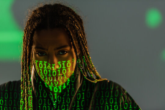 Portrait of african american woman with projection of binary code looking at camera on grey background.