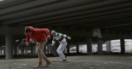 Two young men performing cartwheels and parkour side flips together under urban road bridge - Powered by Adobe