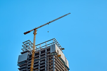Top of yellow tower crane on skyscraper construction against clear blue sky, bottom view
