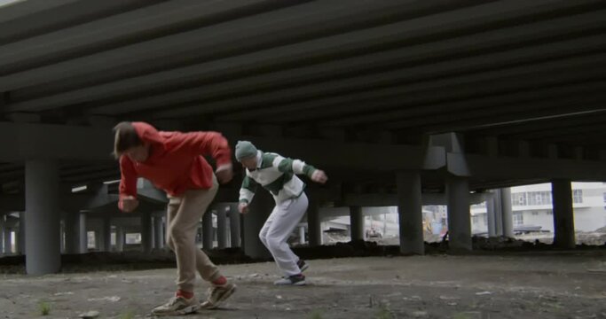 Two young men performing cartwheels and parkour side flips together under urban road bridge