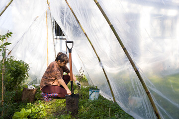Mujer latina trabajando la tierra en un pequeño invernadero urbano. Concepto de huerta propia en...