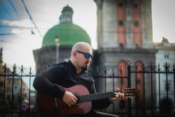 Interesting bearder man wearing sunglasses playing guitar on the street. retro style. Lifestyle, real people concept.