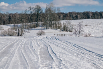 Wooden bridge between the slopes of the hilly area in winter with tracks on the snow and trees in the background.