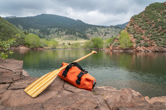 wooden canoe paddle and waterproof duffel on a rocky shore of mountain lake - Horsetooth Reservoir in northern Colorado