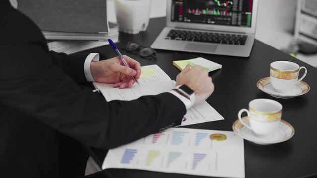 Close-up of male hands writing information in a magazine. A business man working in an office takes notes by hand.
