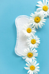 Obraz premium Menstruation period concept. Hygienic white female pad with chamomile flowers on blue background. Menstruation, protection. Women's health