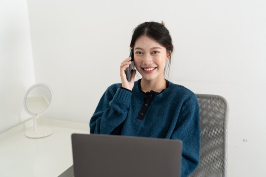 Portrait of smiling beautiful business asian woman using laptop computer and calling byh mobile phone from home concept