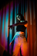 Fototapeta na wymiar Young and sexy woman with wearing jeans and black t-shirt posing in colorful neon light