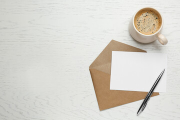 Envelope with blank paper card, cup of coffee and pen on white wooden table, flat lay. Space for...