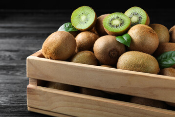 Crate with cut and whole fresh kiwis on black wooden table, closeup