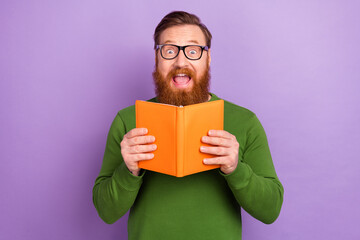 Photo of positive overjoyed young man spend free time with reading story book isolated on violet...