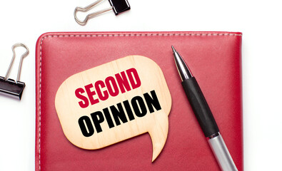 On a light background there are black paper clips, a pen, a burgundy notepad a wooden board with the text SECOND OPINION