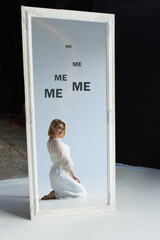 A blonde woman in a white dress admires herself in the mirror, the concept of narcissism and...