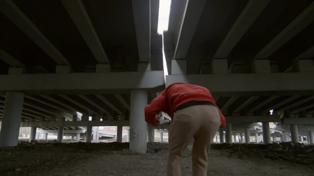 Parkourist running towards the camera, doing cartwheel and performing backflip while training under urban bridge