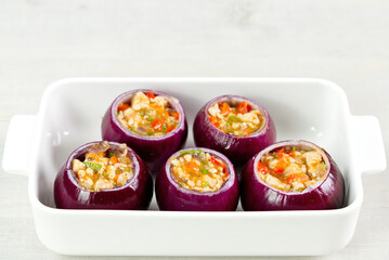 Stuffed onions recipe. Red onions stuffed with meat and vegetables in white bowl ready to bake in the oven. close up