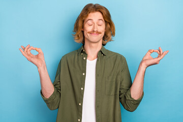 Portrait of attractive funky cheerful guy meditating showing om sign isolated over bright blue...
