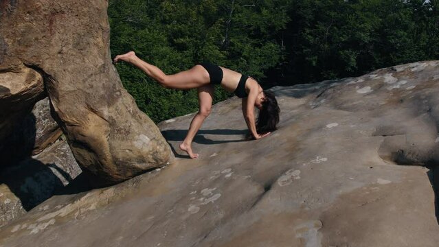 Pretty woman balances stands on her hands. Young beautiful sports lady training at dawn on rocky terrain. Pretty fitness girl in sportswear during workout session on rocky outside.