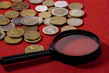 Coins and a magnifying cloth on a red cloth close-up.