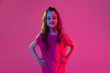 Obraz na płótnie Canvas Portrait of cute little girl, kid wearing pink t-shirt posing isolated on magenta color background. Concept of children emotions, fashion, beauty, school and ad concept