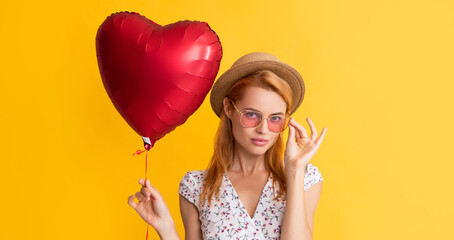 Obraz na płótnie Canvas happy girl in sunglasses hold love heart balloon on yellow background